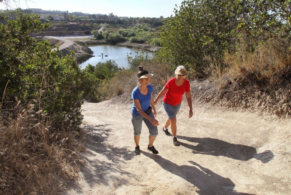 Two friends hike up a steep trail near Lake Calavera in Carlsbad in 2019. A lawsuit alleges the city needs more parks.