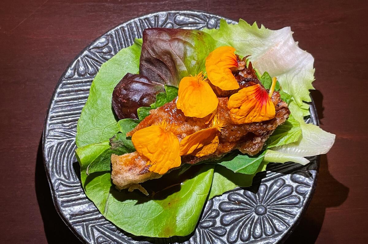 A piece of fried crab sits on a bed of lettuce with orange flower petals on top from Baroo Los Angeles