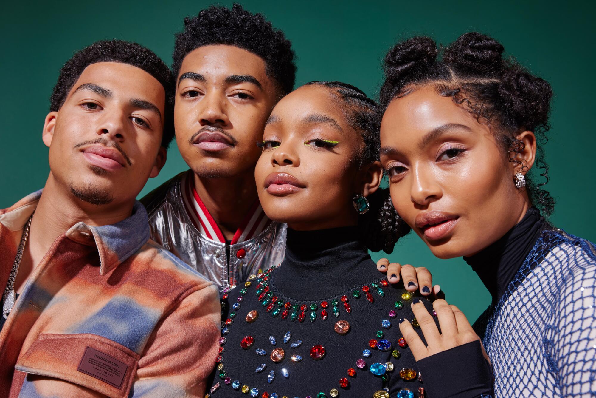 A group of four young adults pose for a portrait in fancy clothing against a green backdrop.