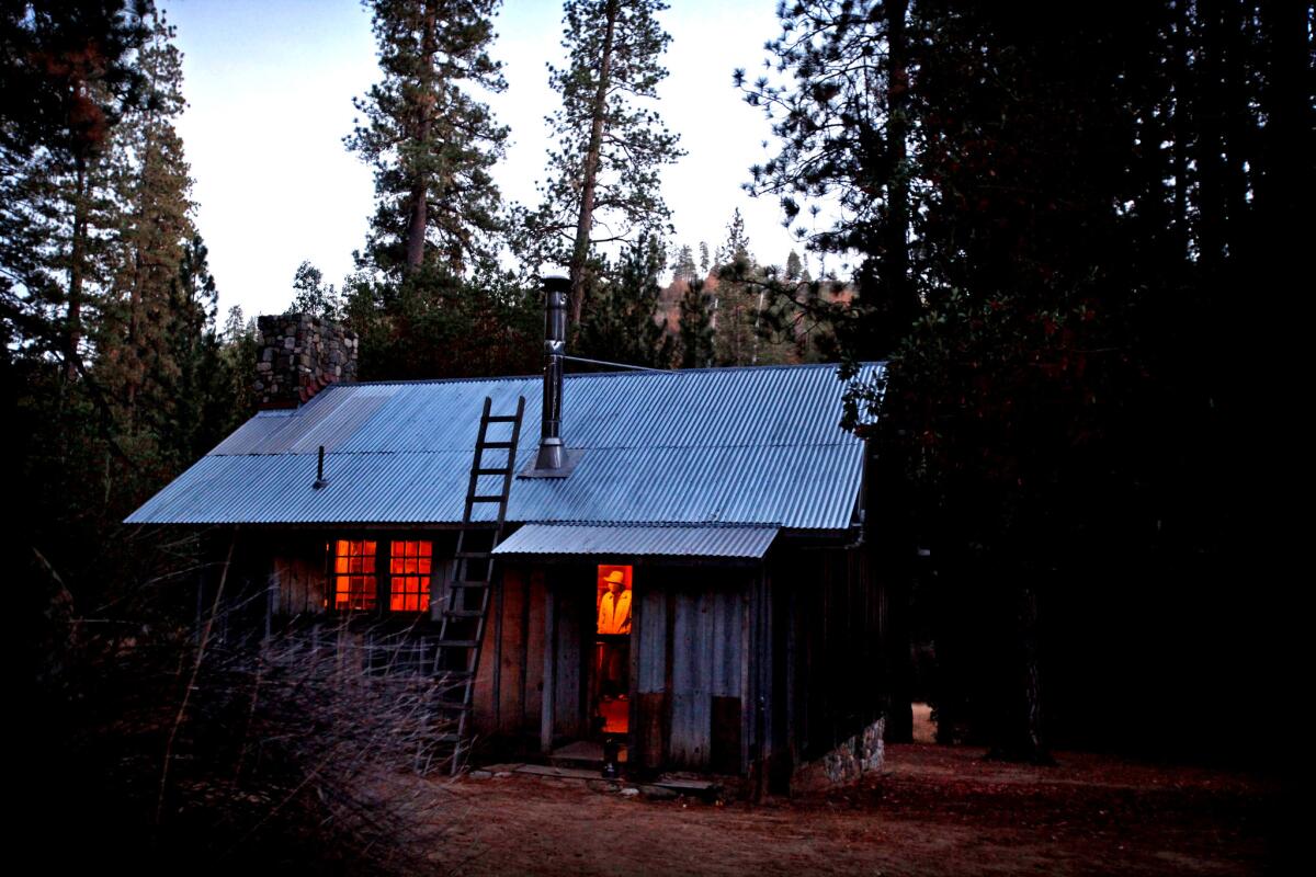 Twilight comes early to the valley in the fall, and the small cabin is lit by the fire and few Coleman lanterns. Jack English's son, Dennis, wanders in front of the open back door. Over the years, English has become something of a legend in the Ventana Wilderness. (Barbara Davidson / Los Angeles Times)