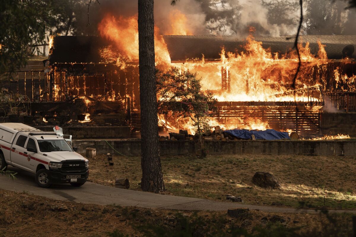 A white truck near a structure engulfed in flames.