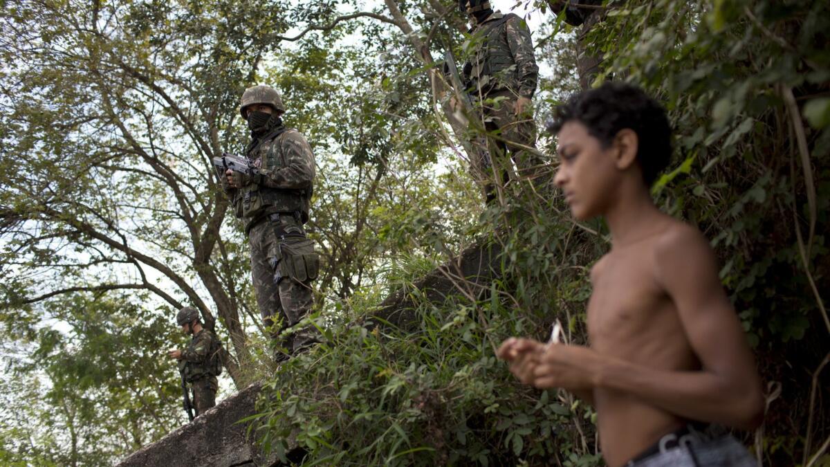 A young boys stands by as Brazilian soldiers patrol a forest area where bodies were allegedly found.
