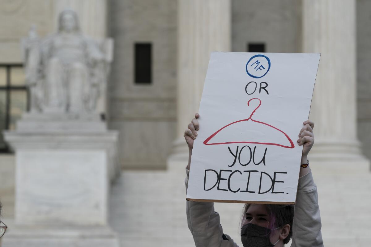 A demonstrator holds up a sign contrasting a coat hanger with a medical pill