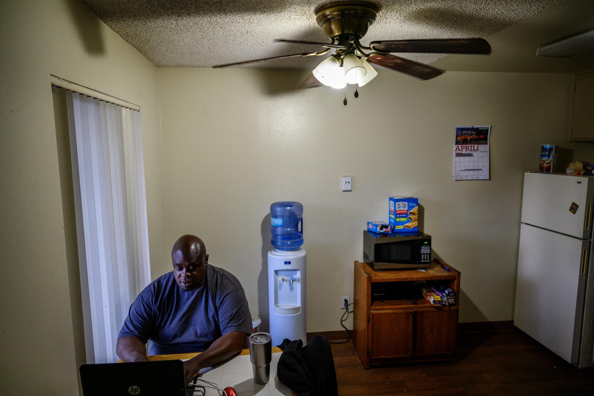 A man uses a computer at a small table in a kitchen area.