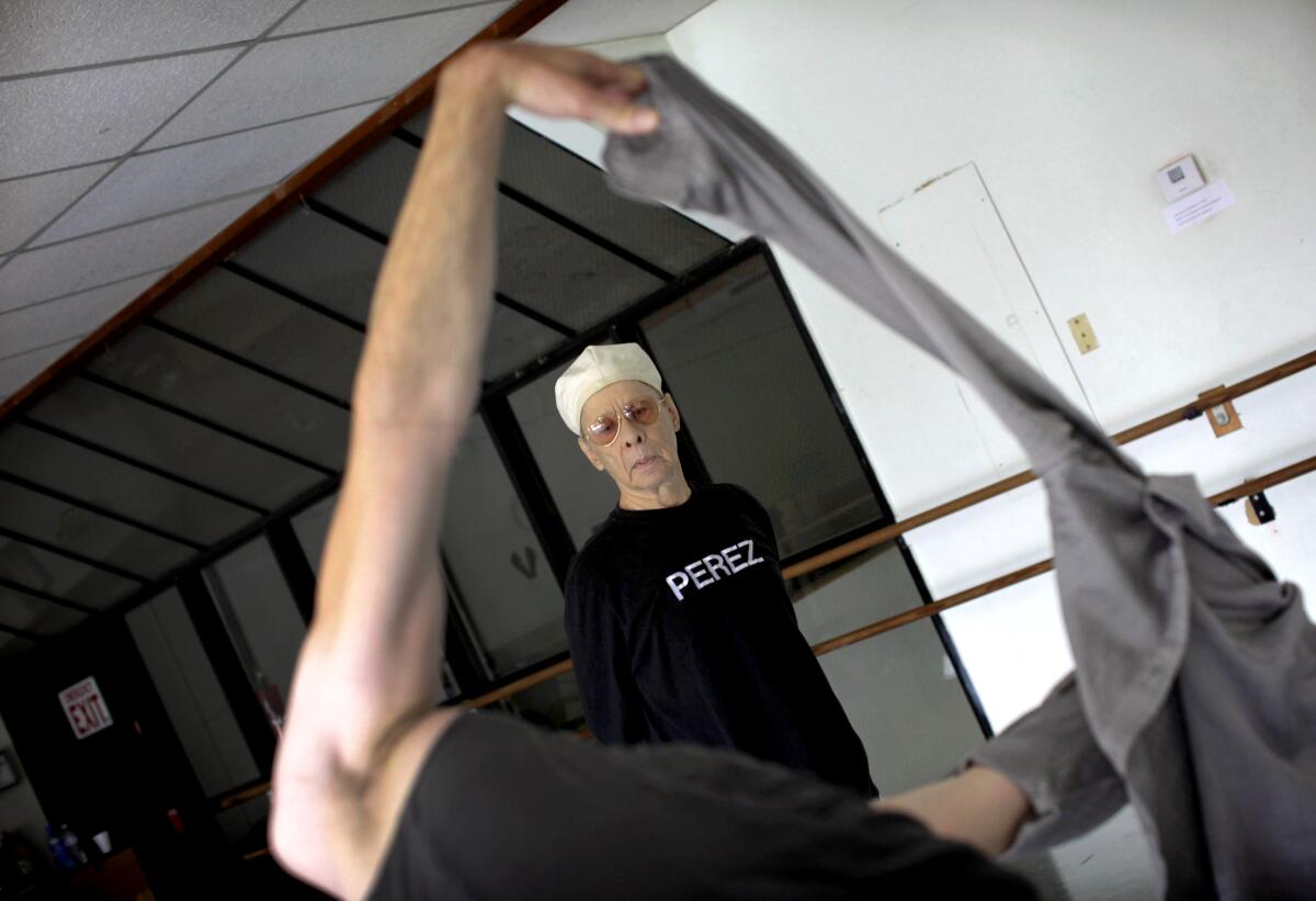 Choreographer Rudy Perez, in a T-shirt that reads "Perez," is seen past a dancer's extended arm during a rehearsal. 
