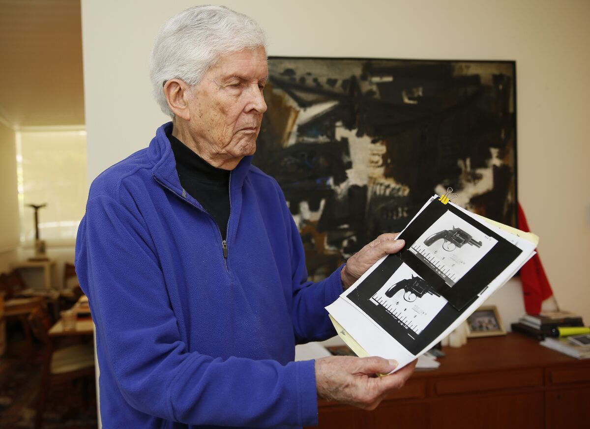 A white-haired Paul Schrade holds photos of a gun.
