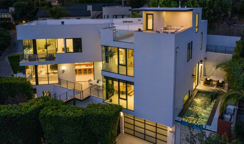 A white two-story building has large glass windows and a pool on the side of the house. It's shown at dusk.