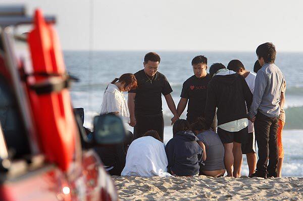 Members of the Laotian Evangelical Church of Banning pray for two friends missing off Huntington Beach Pier on Saturday.