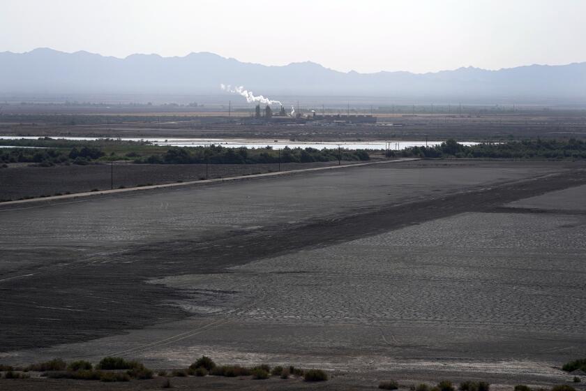 FILE - A dried up portion of the Salton Sea stretches out with a geothermal power plant in the distance in Niland, Calif., Thursday, July 15, 2021. Demand for electric vehicles has shifted investments into high gear to extract lithium from geothermal wastewater around the rapidly shrinking body of water. The ultralight metal is critical to rechargeable batteries. (AP Photo/Marcio Jose Sanchez, File)