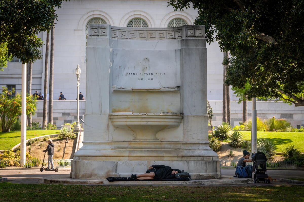 People sleep and rest on a fountain in the shade outside City Hall