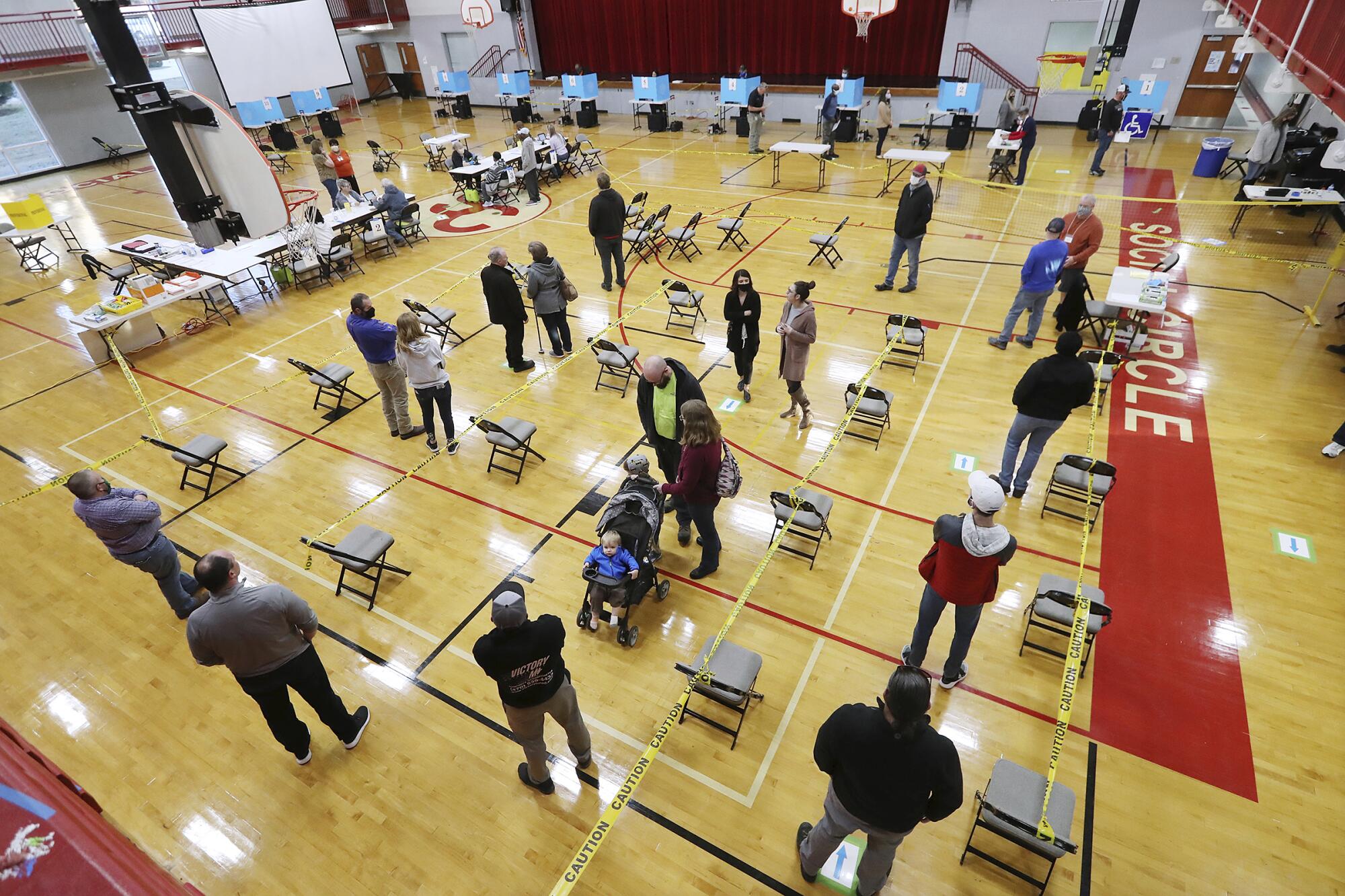 Yellow caution tape held up by folding chairs delineates waiting lines for voters on a school gymnasium floor.