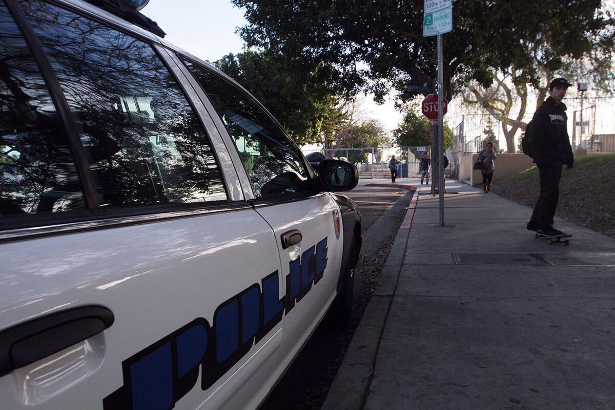 A skateboarder passes an LAUSD School Police car on his way to class Wednesday as students return to San Pedro High School.