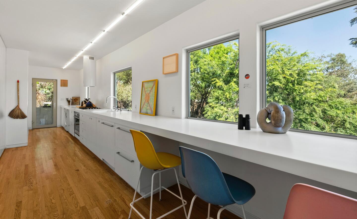 The kitchen with a long counter, chairs and windows overlooking trees.