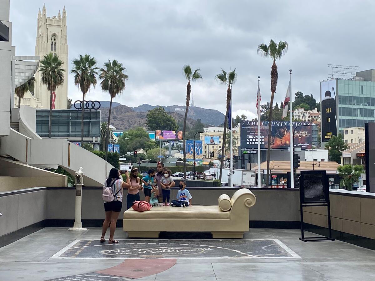 People pause for photos near a daybed sculpture with the Hollywood sign in the background.