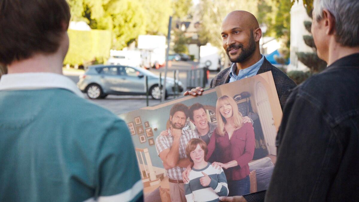 A smiling man shows a large photo of a group of people in "Reboot."