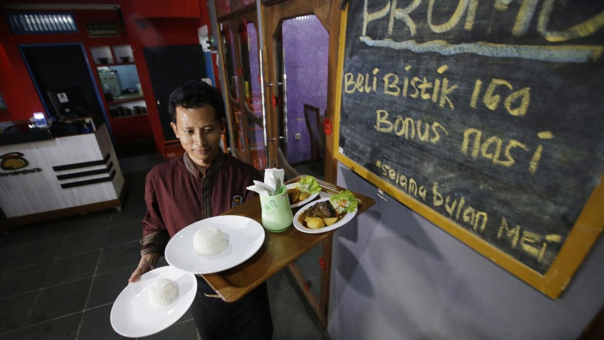 Machmudi Hariono carries a tray of food for customers at his restaurant in Solo, Central Java, Indonesia.