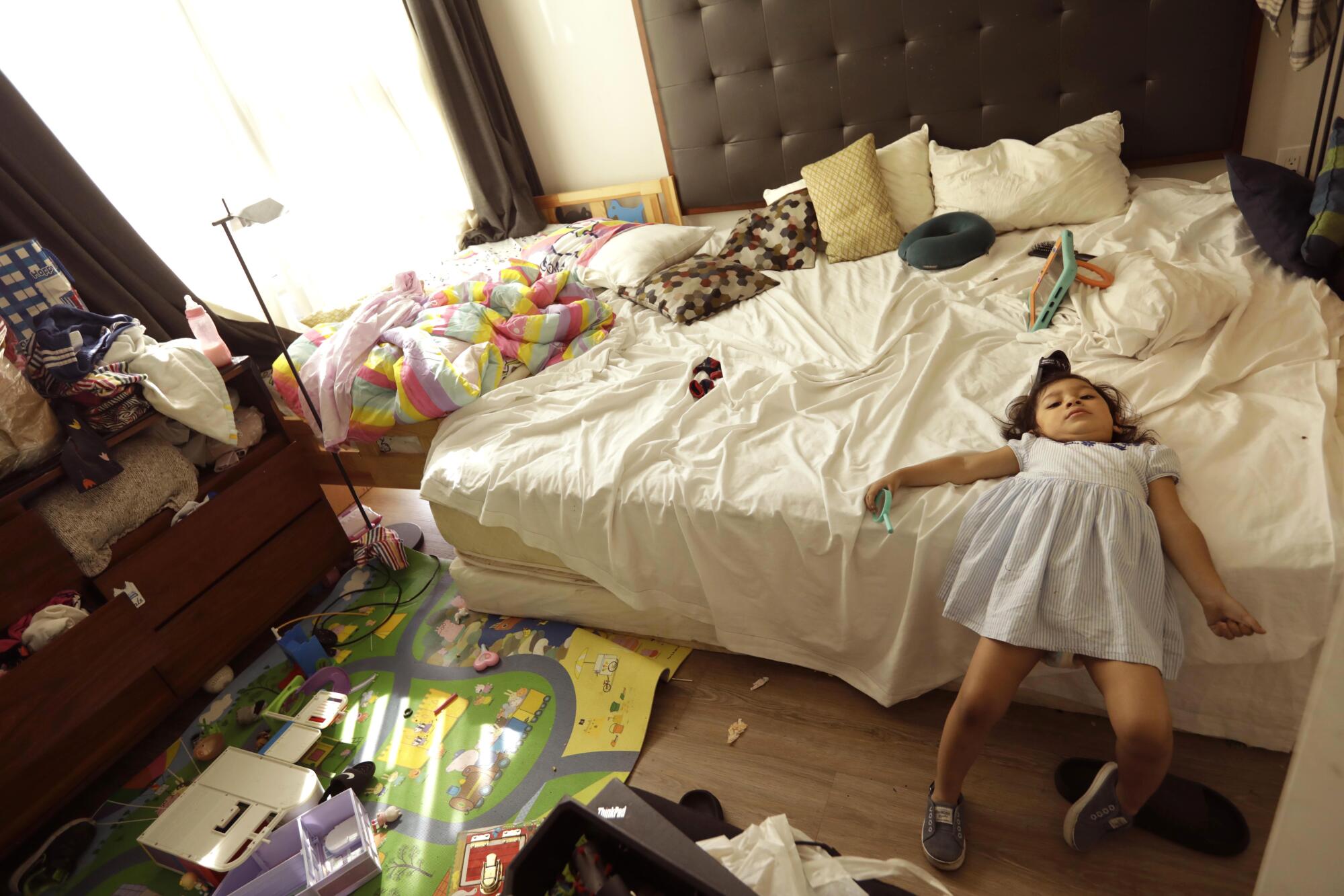 A young girl lies on a bed next to toys