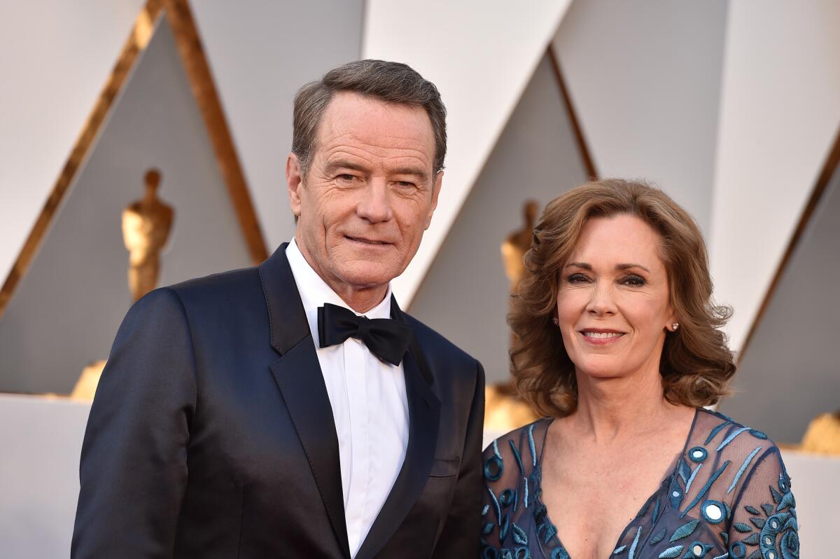 Bryan Cranston wears a tuxedo and stands next to his wife, Robin Dearden, who wears a blue mesh gown.