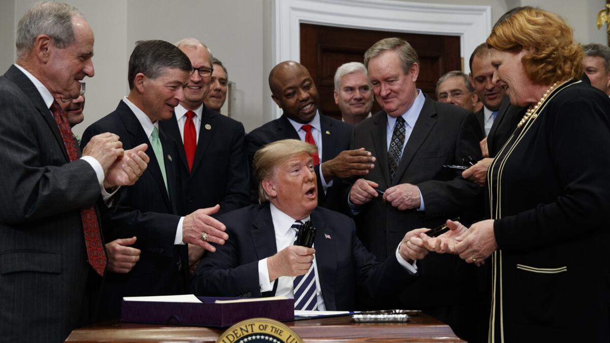 President Trump hands out pens to Sen. Heidi Heitkamp (D-S.D.), right, and other lawmakers after signing legislation rolling back some Dodd-Frank financial regulations at the White House on Thursday.