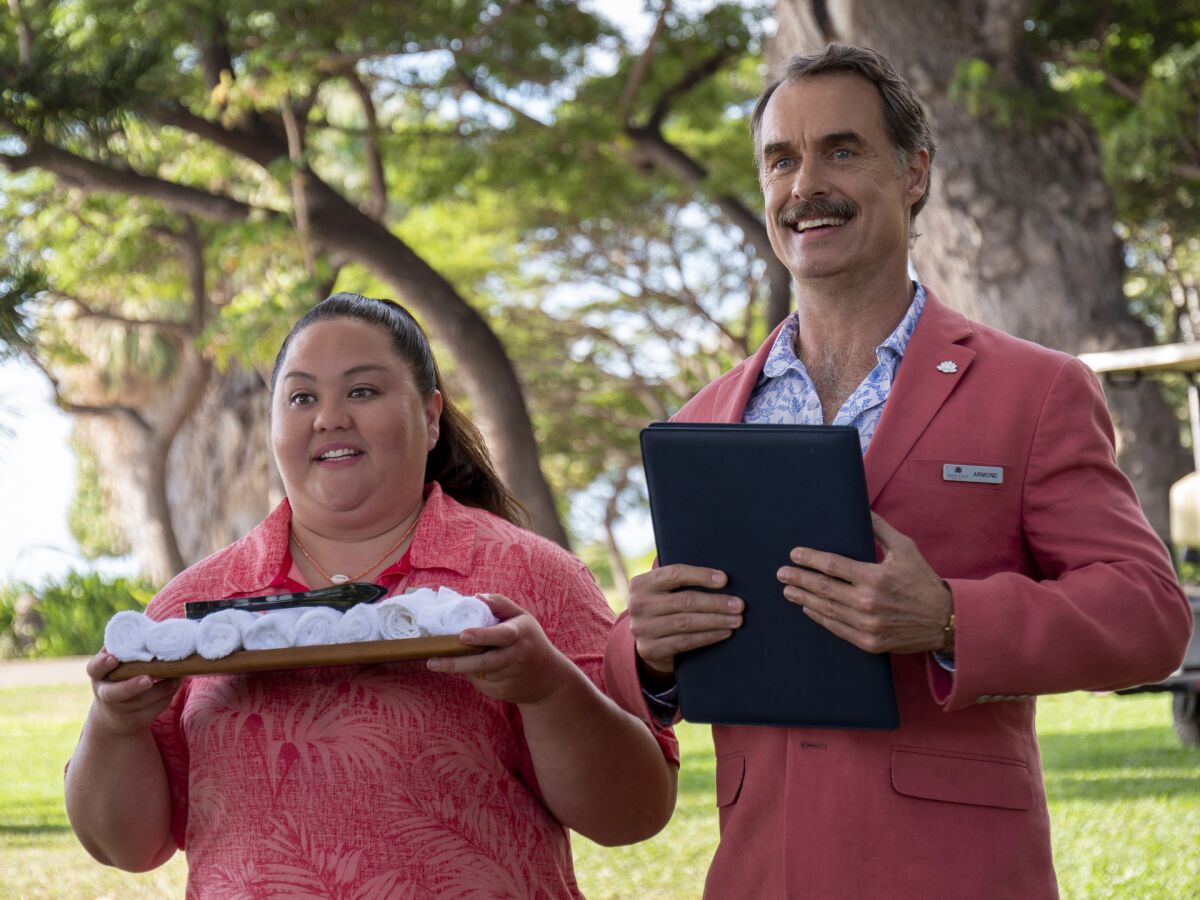 A woman holding a tray of rolled towels and a man holding a clipboard stand outdoors looking expectant.