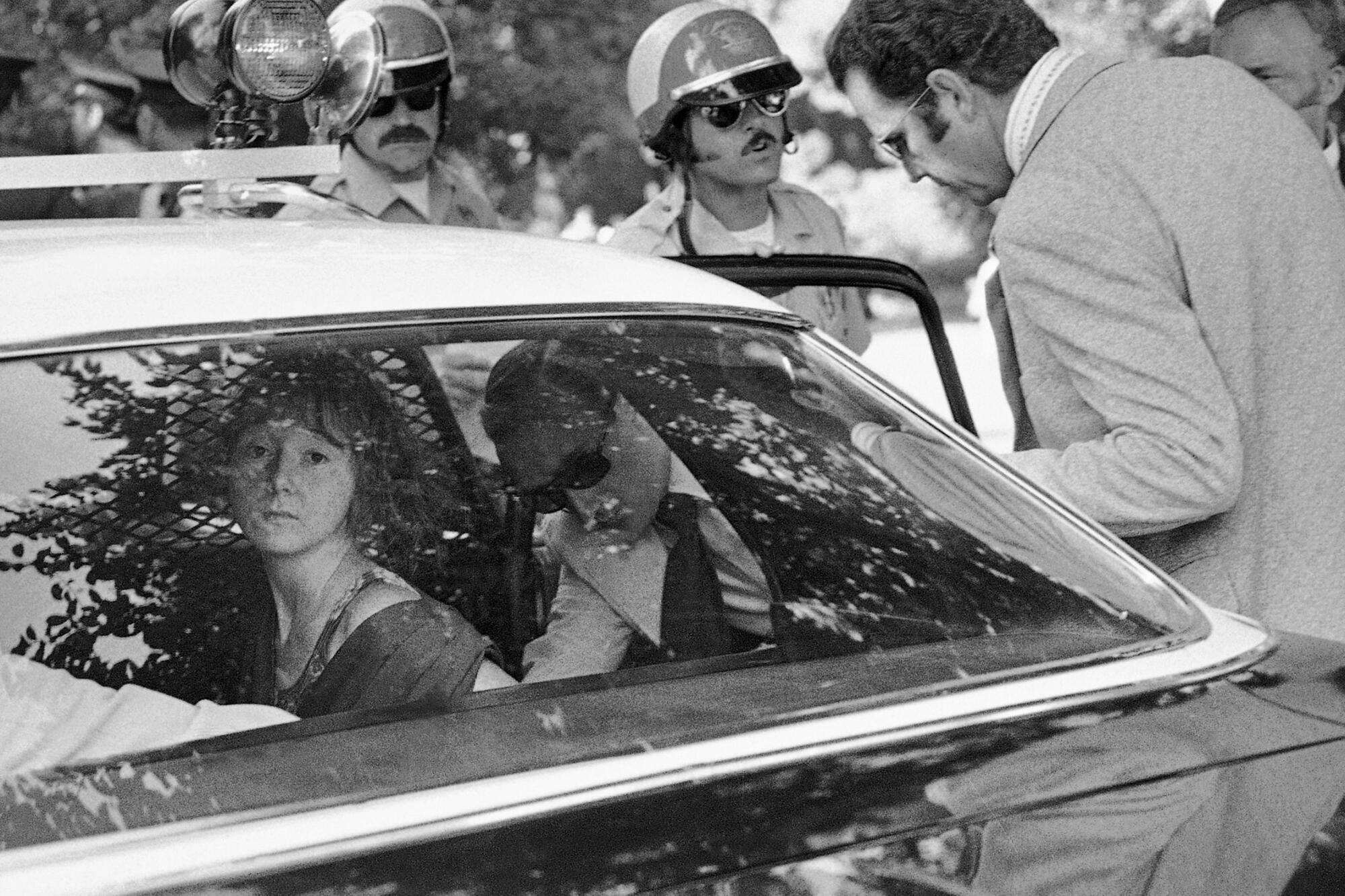 A young woman stares out the back window of a police car.