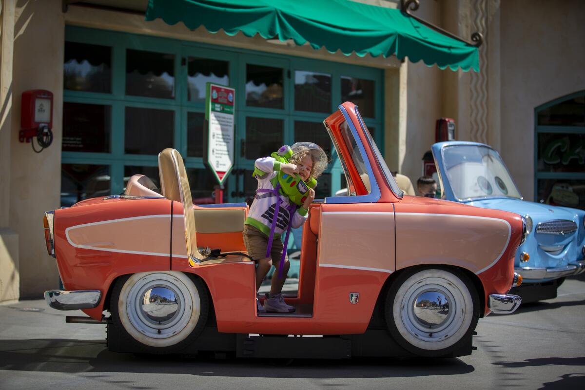 A boy in a Buzz Lightyear costume stands in a miniature car in Cars Land.