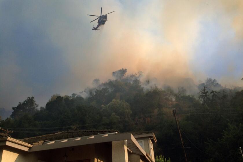 A fire helicopter makes a water drop on a brushfire in the hills behind homes in Glenoaks Canyon on Sunday, August 25, 2019. The fire started in Eagle Rock, jumped the freeway and made its way into Glendale. (Photo by James Carbone)