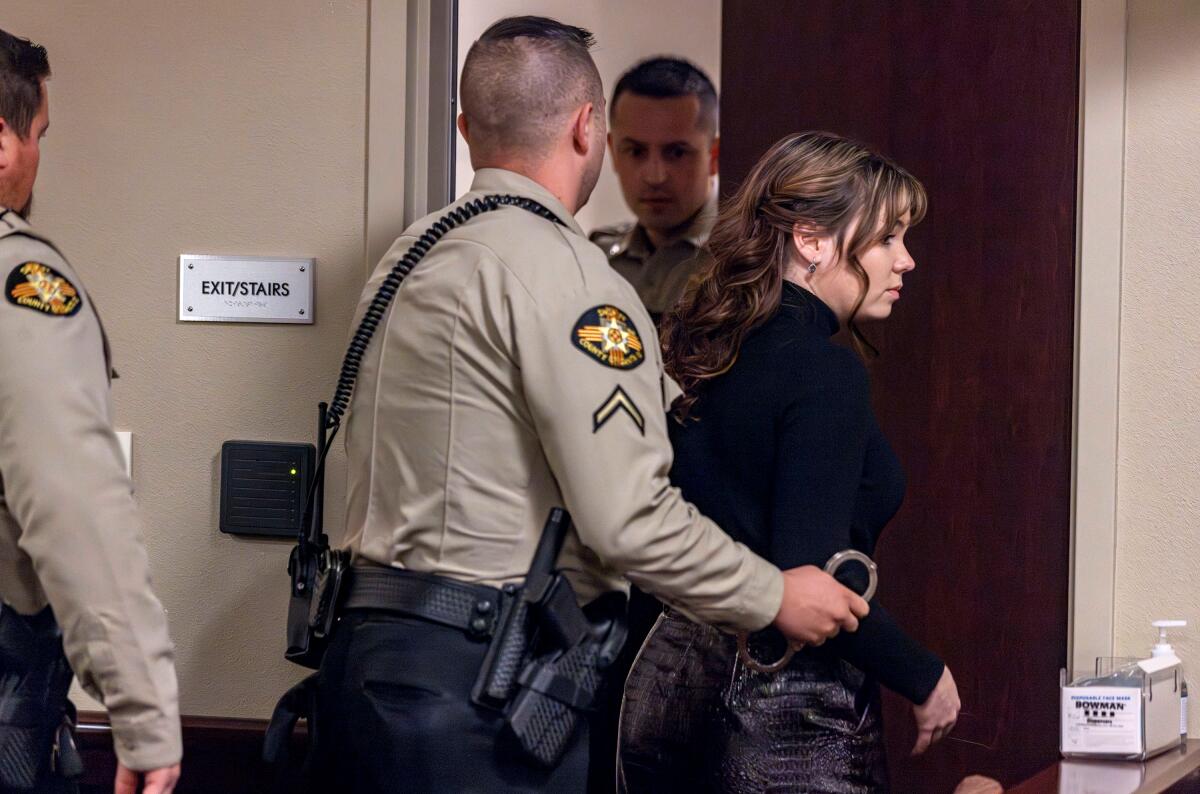 A woman is escorted by law enforcement officers through a door