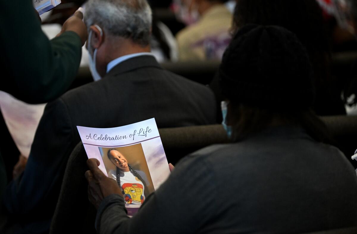 A mourner holds a funeral program with the image of slain teen Tioni Theus.