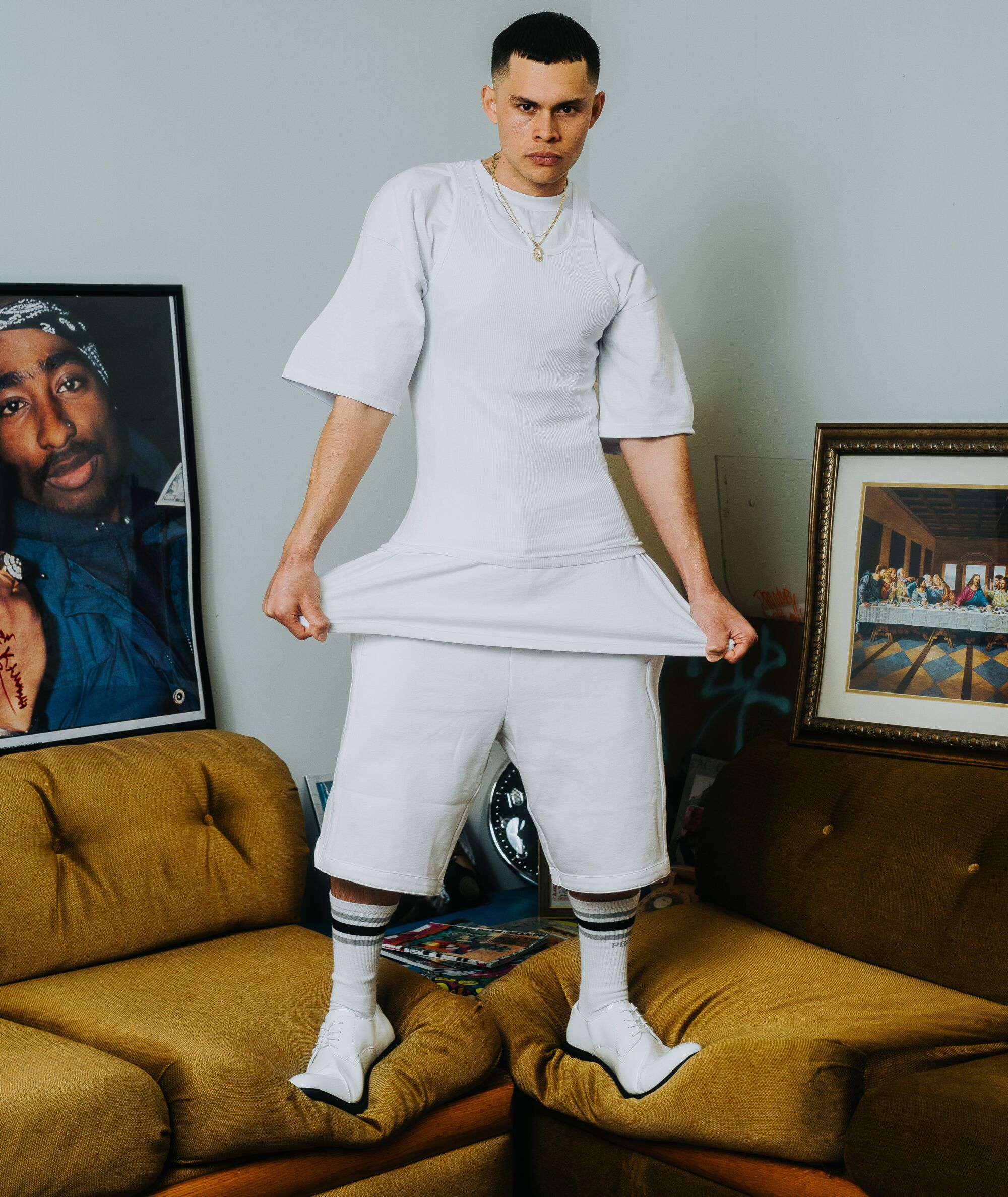 A model wears a full Pro Club outfit while standing on a couch.