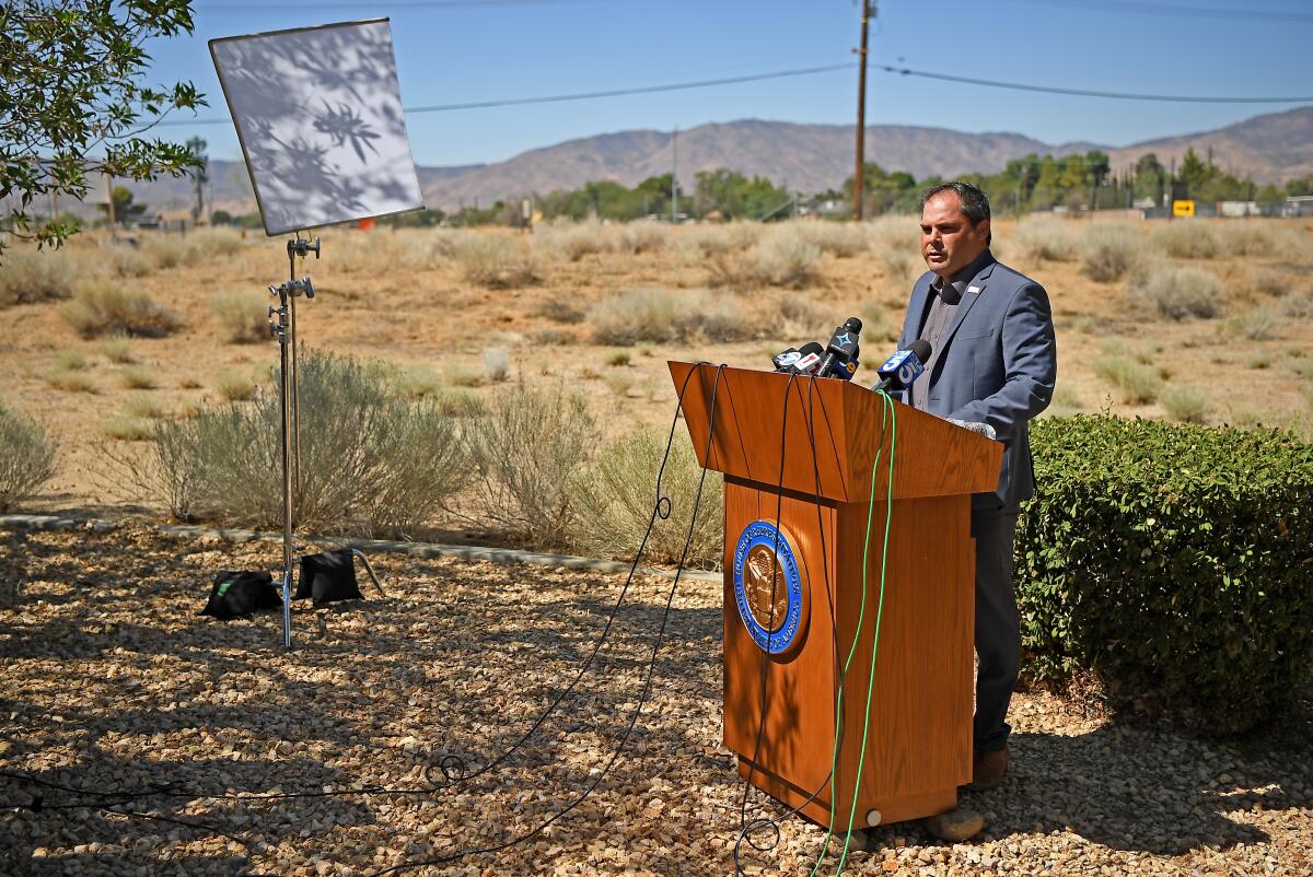 A man in a suit speaks at a podium outdoors.