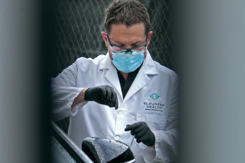 Dr. Matthew Abinante can be seen through the crack of a door putting away a drive-up sample swab for the novel coronavirus COVID-19 from a patient who remained in their vehicle, outside the offices of Elevated Health in Huntington Beach on Thursday, March 19, 2020.