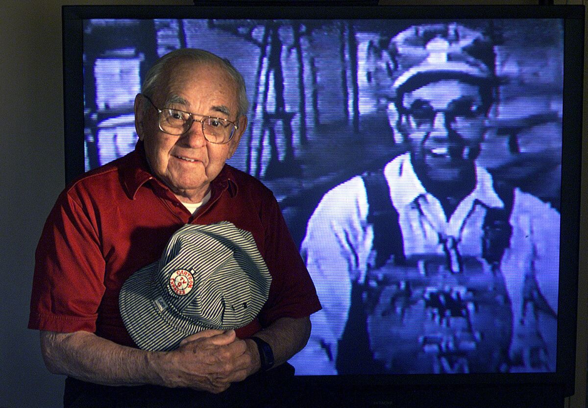 Bill Stulla sits in front of television screen showing videotape of him during his TV show, Cartoon Express with Engineer Bill that ran on channel 9 from 1954-1966.