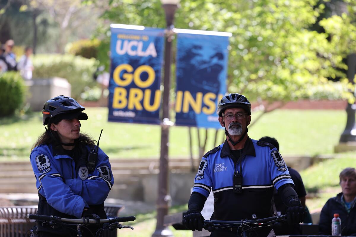 Private security guards with bicycles and blue-black jackets patrol UCLA; behind them, signs reading "Go Bruins!"