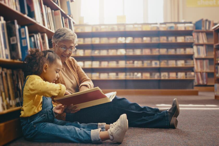 An older adult reads a book with a child in a library.