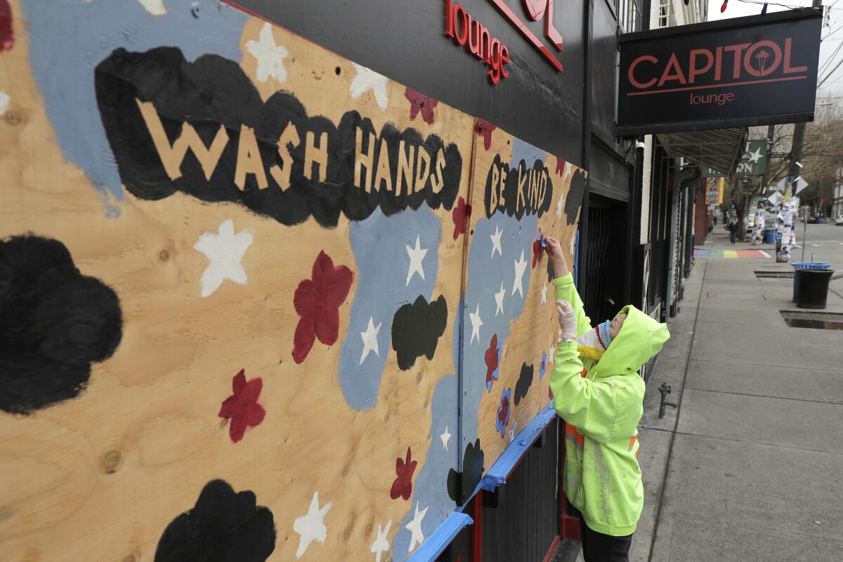 Momo Nikaido applies masking tape to a mural that reads "Wash hands, be kind" over the boarded-up windows of the Capitol Lounge, owned by her father in Seattle's Capitol Hill neighborhood.