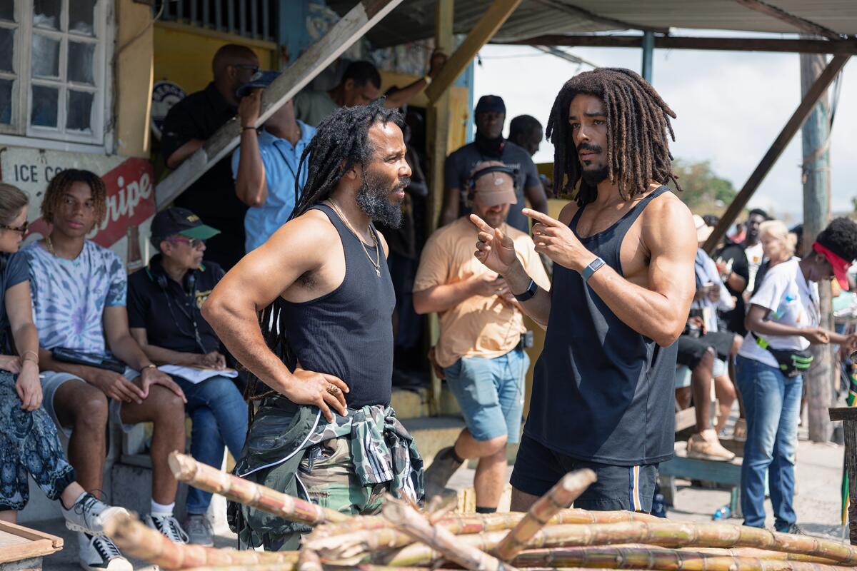 Ziggy Marley and Kingsley Ben-Adir wearing tank tops while standing on the set of a film