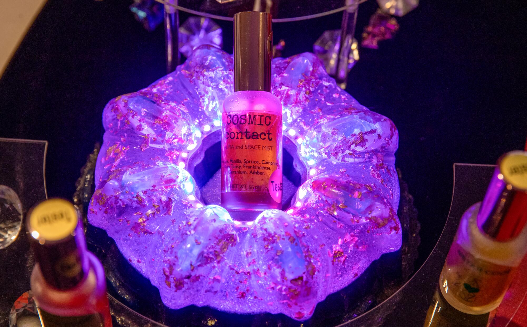 A spray bottle of Cosmic Contact set in a glowing purple doughnut-shaped display