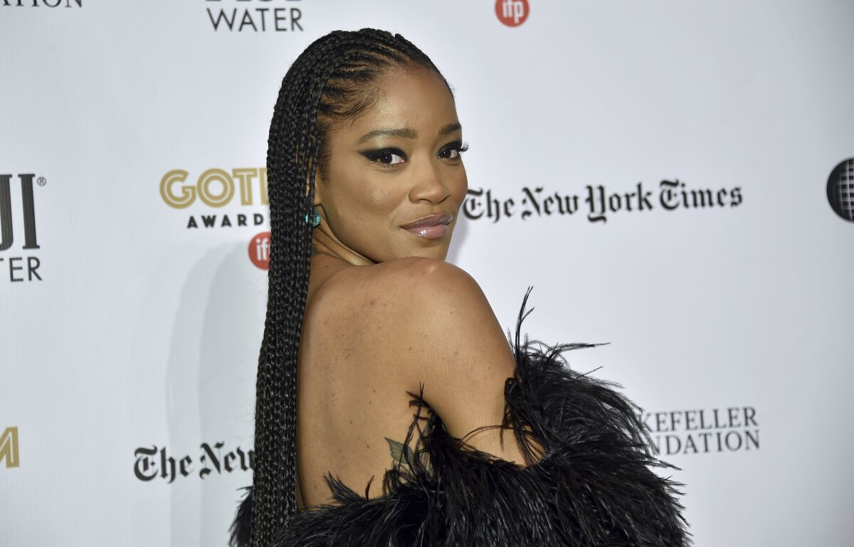 A woman with long, braided hair posing in an off-the-shoulder feathered black dress.
