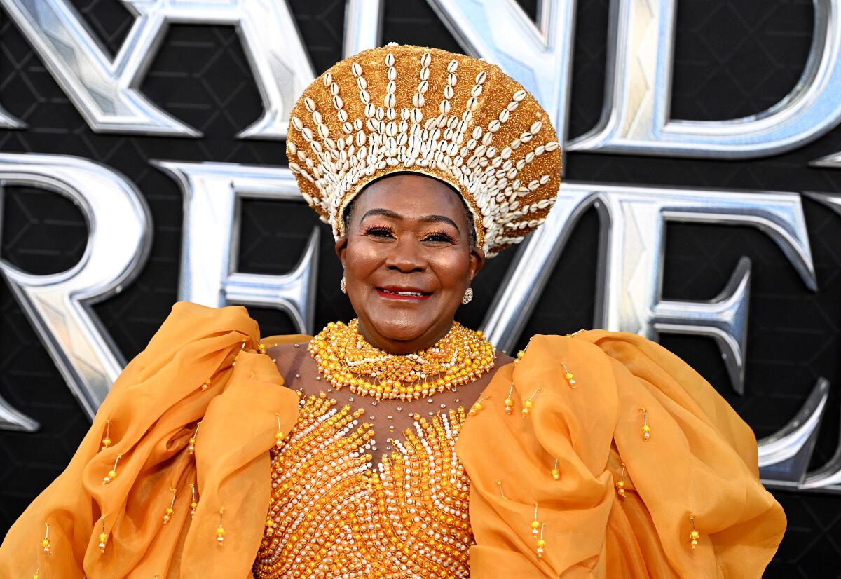 A smiling Connie Chiume wears an orange dress and studded headwear. 