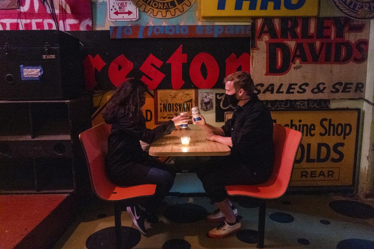 Two people toast beer cans at a bar