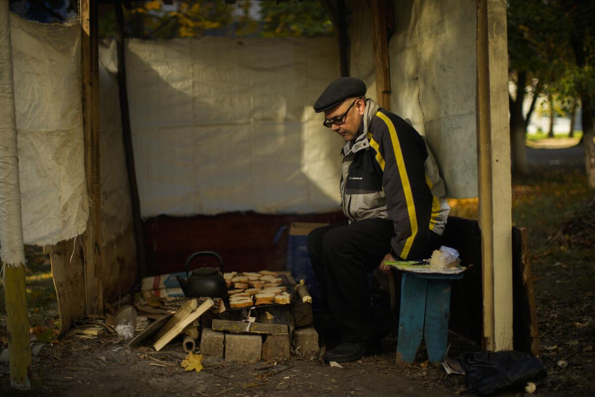 Anton Sevrukov, 47, toasts bread over fire in a makeshift stove in Kivsharivka, Ukraine, Sunday, Oct. 16, 2022. As temperatures drop below freezing in eastern Ukraine, those who haven't fled from the heavy fighting, regular shelling and months of Russian occupation are now on the threshold of a brutal winter and digging in for the cold months. (AP Photo/Francisco Seco)