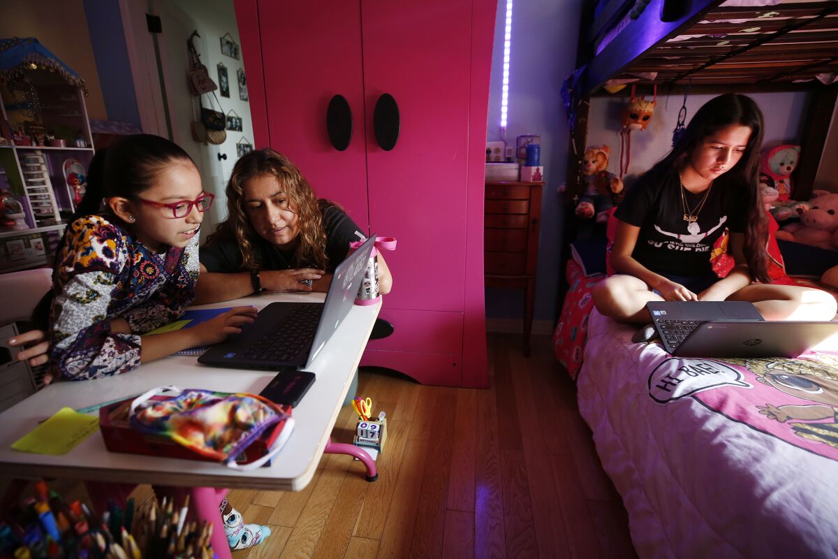 A mom helps her daughters with remote learning on laptops in their bedroom.