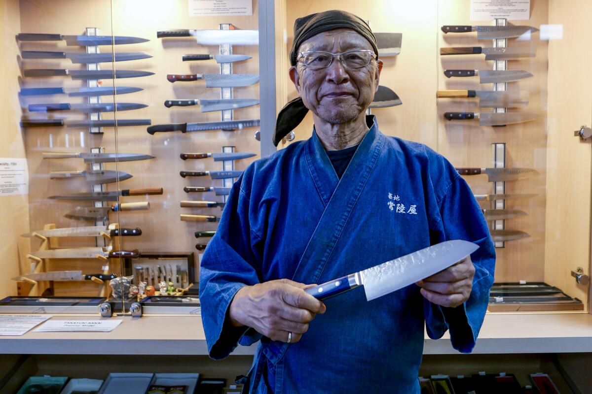 A man stands in front of a case full of chef's knives, holding a knife