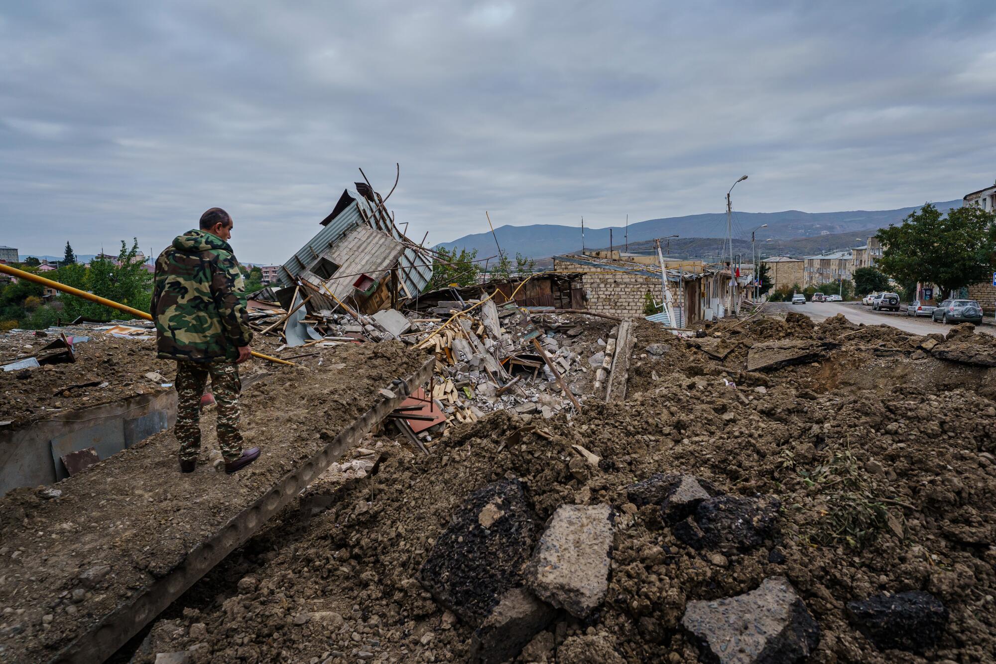 A man looks over a crater blast along a street in front of a residential area in Stepanakert.