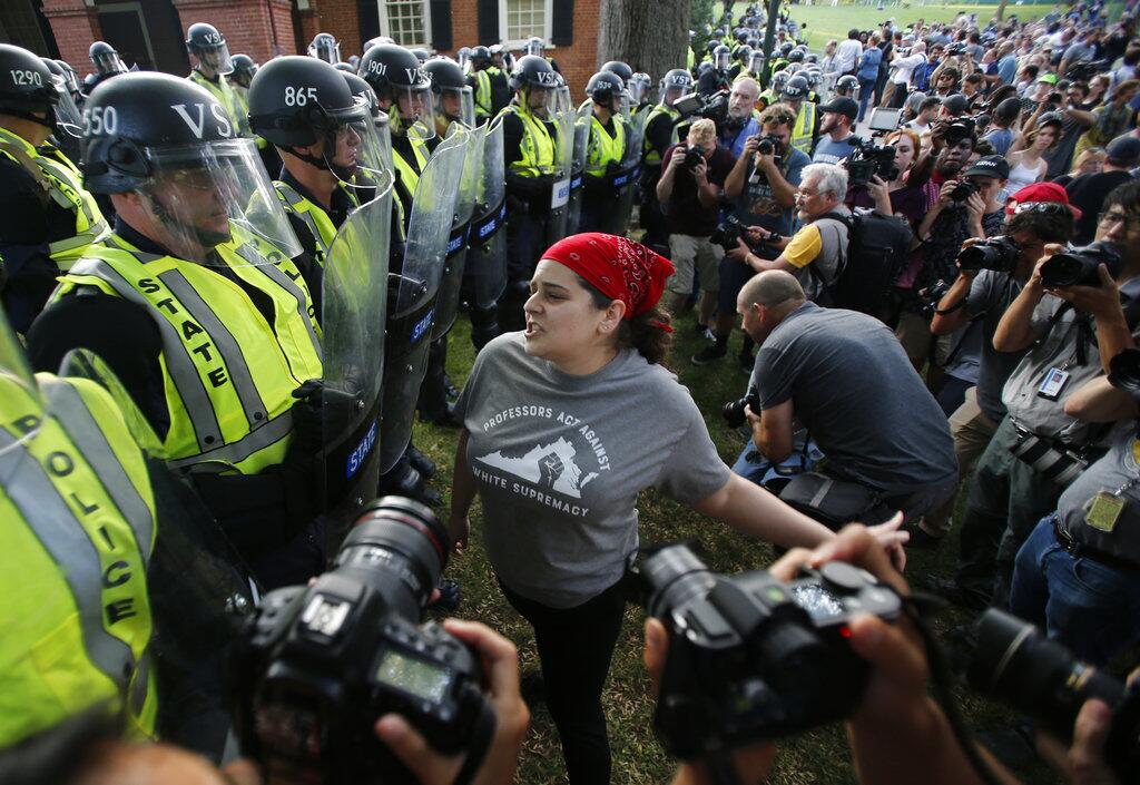 A protester confronts riot gear-clad police on the campus of the University of Virginia during a rally to mark the anniversary of last year's Unite the Right rally in Charlottesville, Va., Saturday, Aug. 11, 2018.