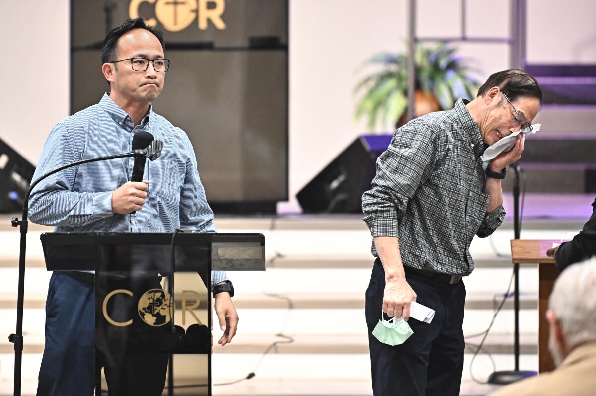 A man stands behind a lectern as a man near him wipes away tears.