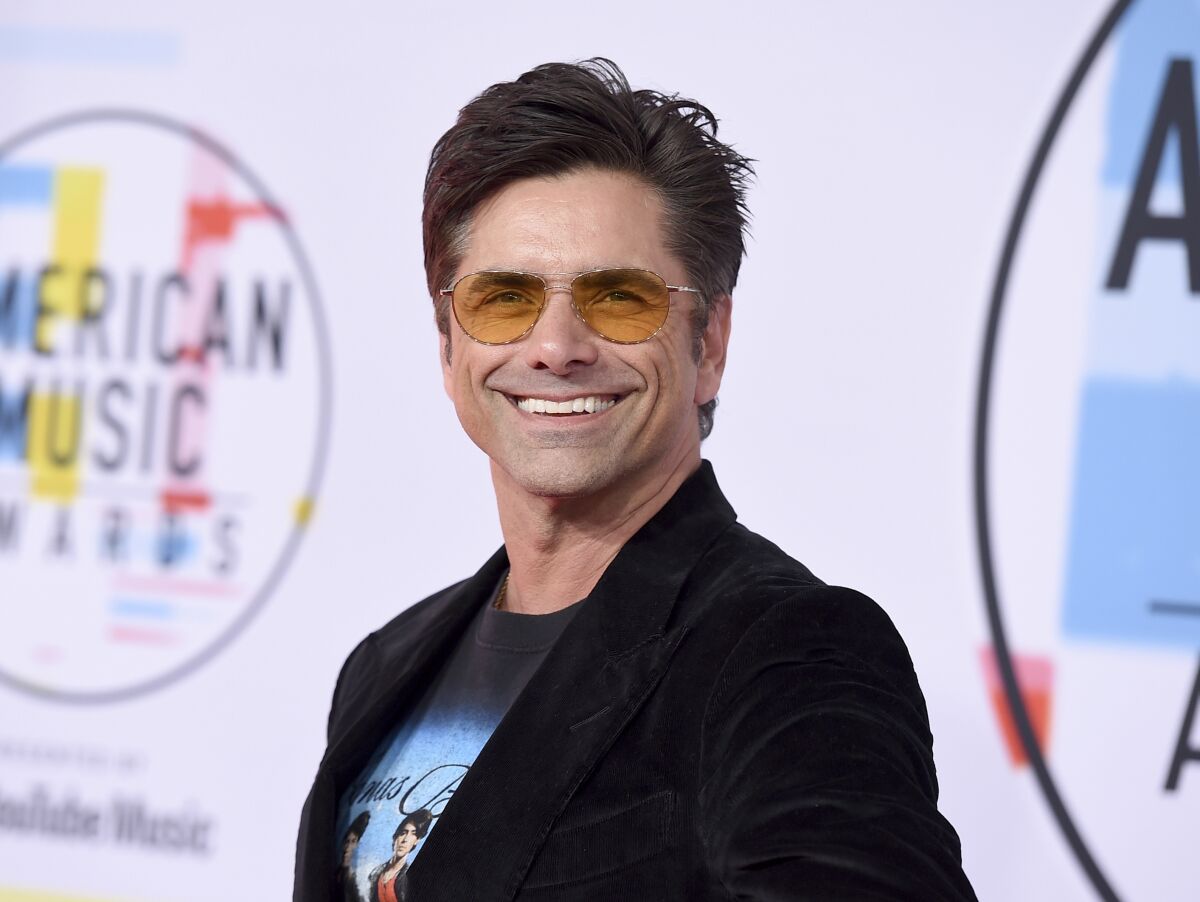 A smiling man with short brown hair and yellow-lens sunglasses