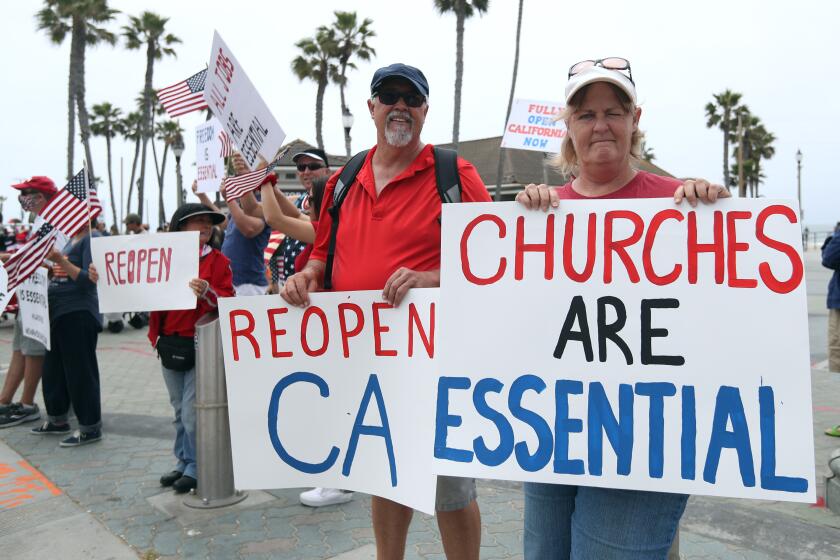 Wally Thomas of Lake Forest, center left, and Denean MacAndrew of Mission Viejo, right, hold signs during the protest at Pier Plaza in Huntington Beach on Saturday.