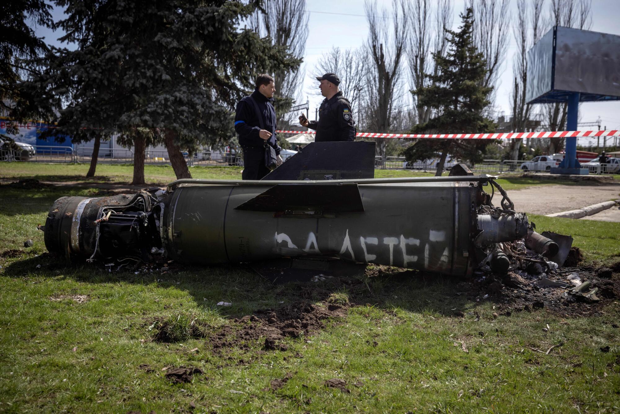 Ukrainian police inspect the remains of a large rocket with the words "for our children" in Russian